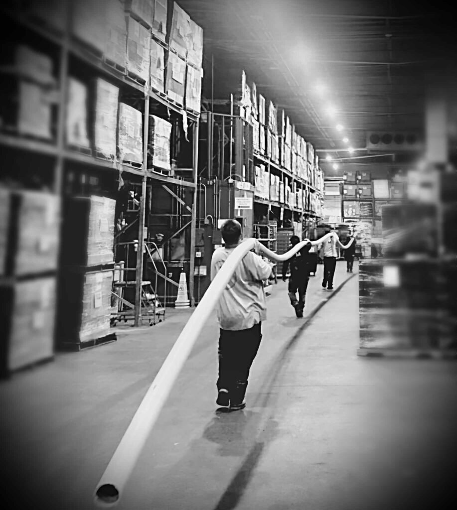 Trenchless sewer line being carried through warehouse by plumbers in Sacramento