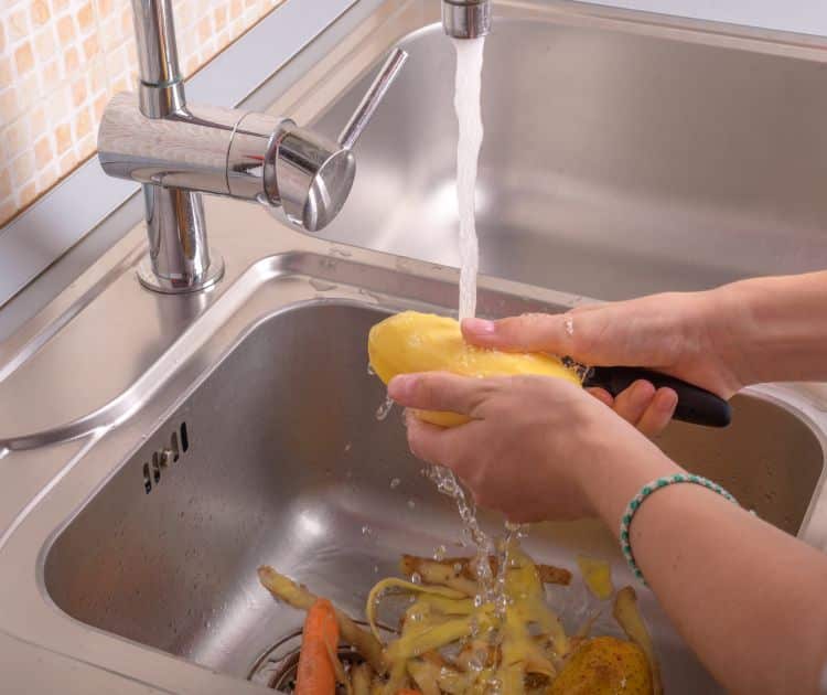 Female hands washing and peeling potatoes over kitchen sink garbage disposal in Sacramento